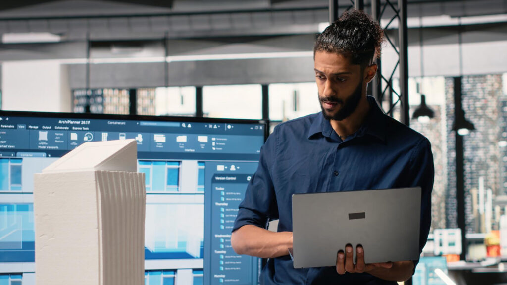 Technicien avec ordinateur portable en salle de supervision industrielle, cybersécurité IT et OT