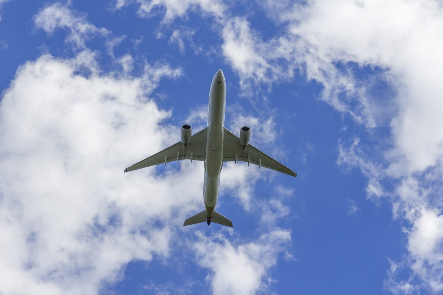 Avion de ligne vu du dessous dans un ciel nuageux, assurance aéronautique