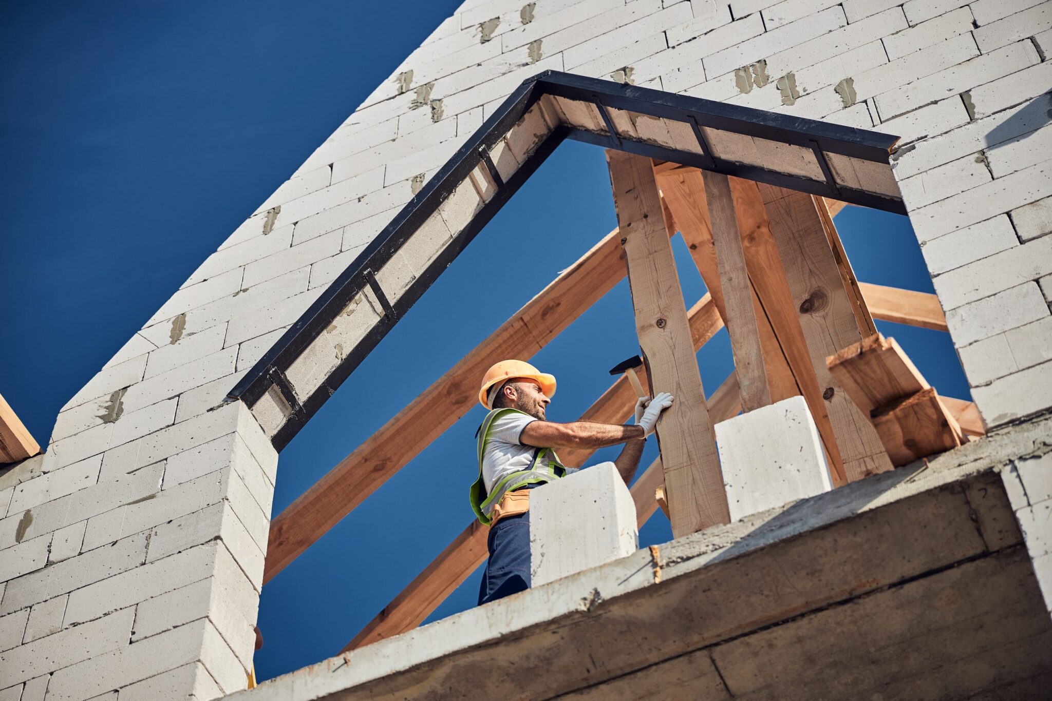 Ouvrier sur une charpente et un mur en parpaings, assurance chantier et gros œuvre